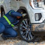 Mechanic working on the wheel of a white off-road vehicle outdoors, fixing a problem.